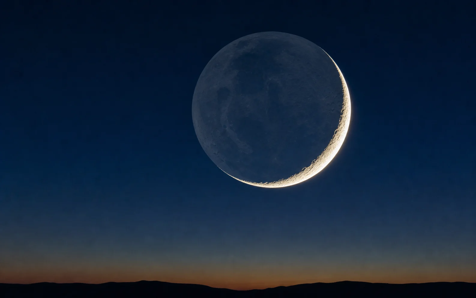 A thin crescent Moon with its night side faintly visible through earthshine.