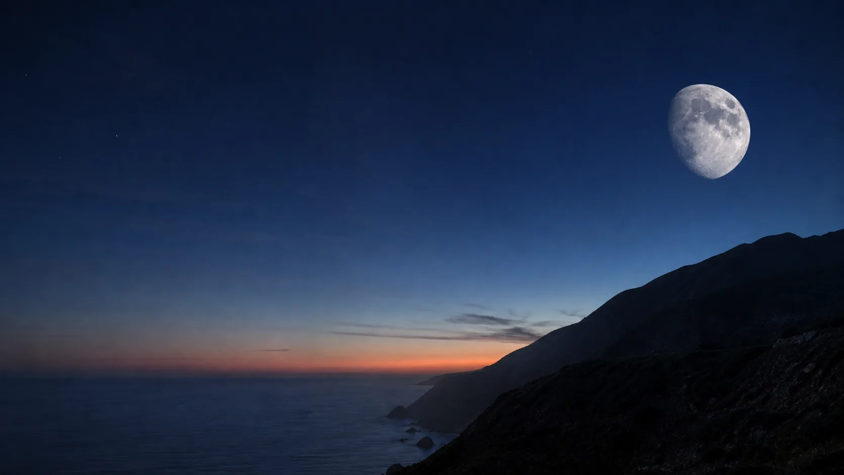 A bright Moon above a dark coastal ridge.